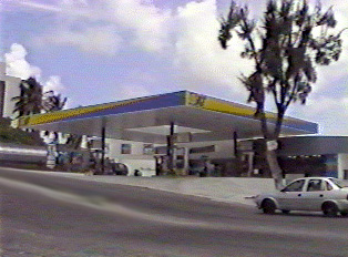 A white car driving on the road alongside a gas station