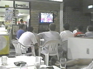 Several men seated around a small table watching TV inside a restaurant