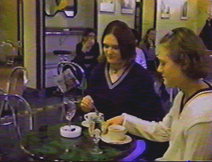 Two people seated in a coffee bar, stirring their drinks