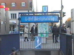 A subway entrance at the corner of a sidewalk, with a blue sign indicating the station name