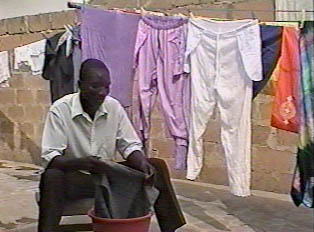A man rinses clothes in a small bin, with a long clothes line with several clothing items hung up behind him