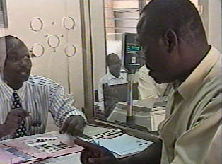 A customer stands at a booth inside a post office, purchasing stamps from the worker behind the counter