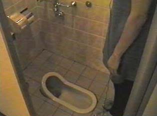 A person standing over a toilet in a public restroom