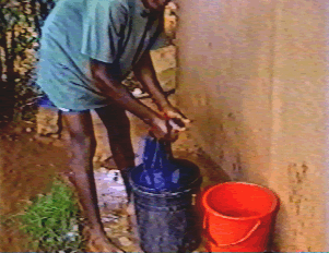 A person bent over a bucket outdoors, doing laundry by hand