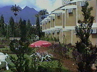 The outside of a hotel, with lush green plant-life and mountains in the background