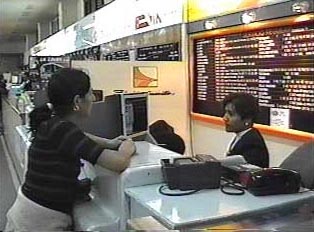 A woman talking to an attendant behind the counter at a bus station, asking to purchase a bus ticket