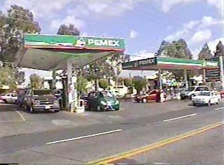 A gas station called 'Pemex' with several cars parked at gas pumps, purchasing gas