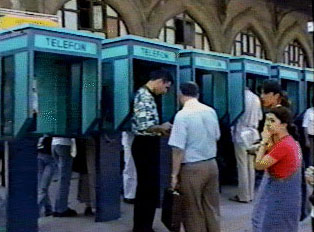 A line of blue phone booths, surrounded by several people