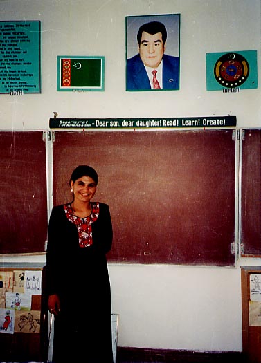 Highschool classroom in Turkmenistan and teacher in traditional clothes (in the backround are national symbols: picture of the president, hymn, flag and emblem