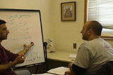 a student and a language mentor talking to each other in front of a white board